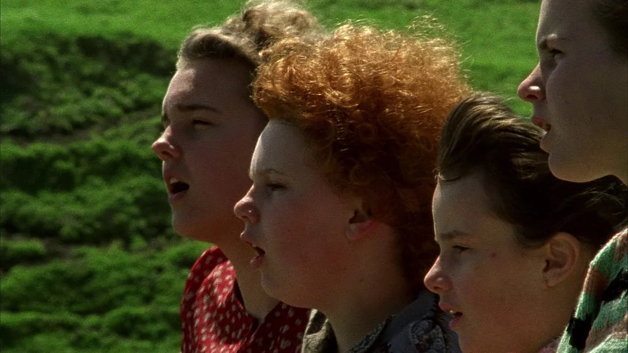 An Angel At My Table (1990) movie still: closeup — Three young women stand in a row against a bright green grassy hillside. They are positioned in…