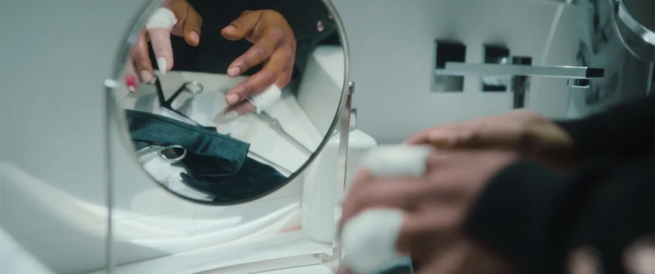 Phobias (2021) movie still: closeup — A clean white bathroom vanity features a small circular mirror and surgical tools. A person with bandaged…
