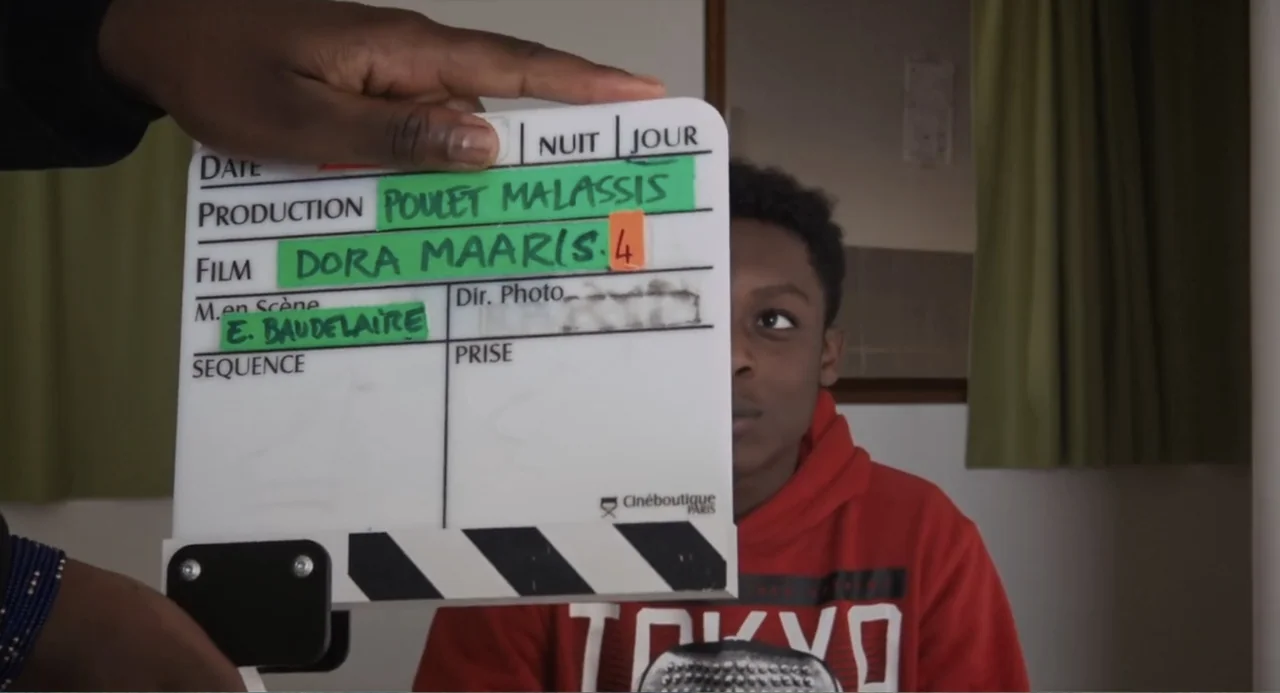 A Dramatic Film (2019) movie still: medium — An interior space features a green curtain backdrop and white walls. A person holds a white production…