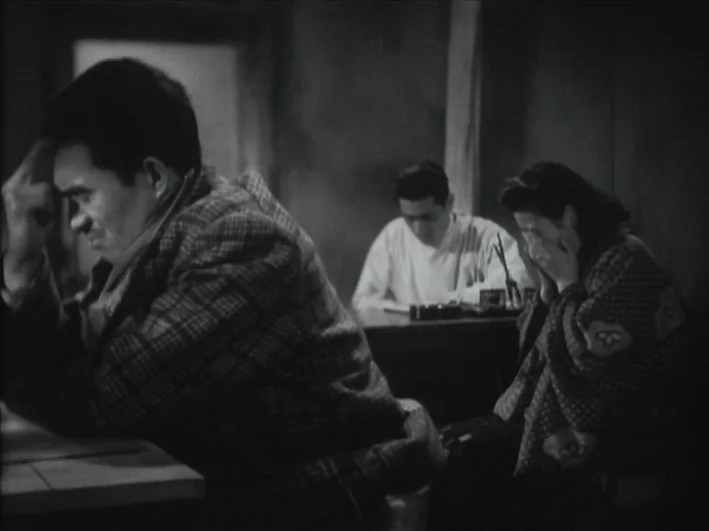 The Quiet Duel (1949) movie still: medium — A dimly lit office features a man in the foreground and a woman nearby. A third person sits at a desk in…