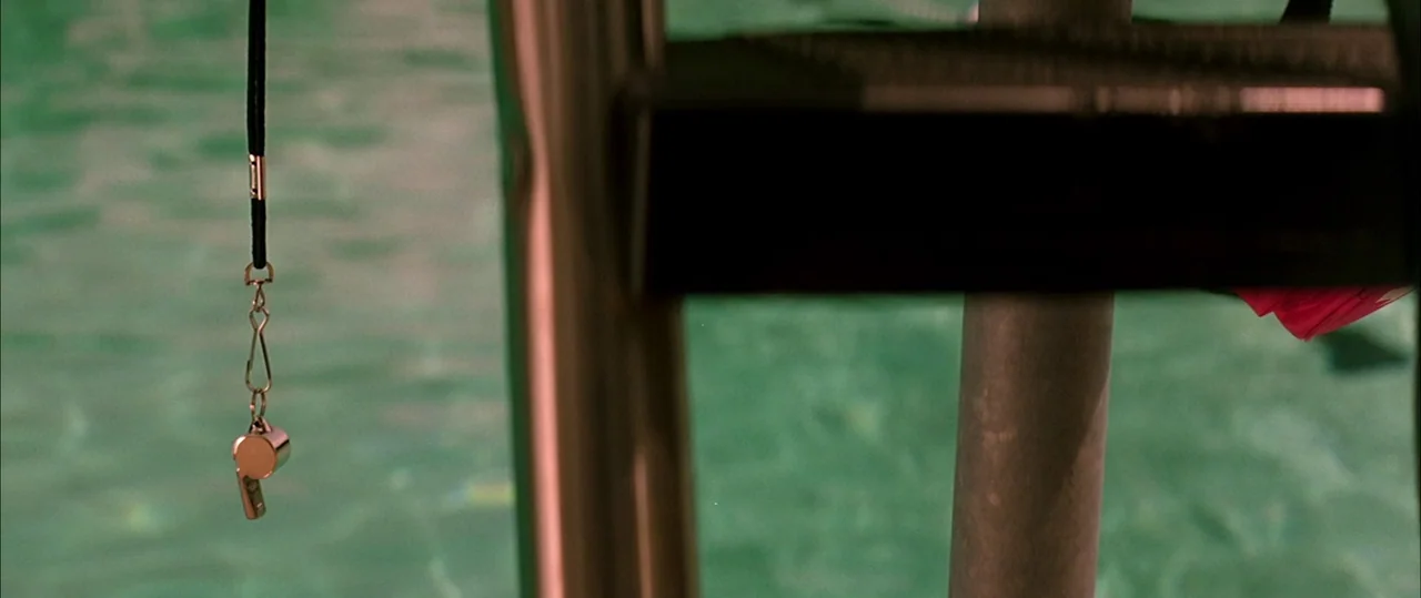 George Washington (2000) movie still: closeup — A metal whistle hangs from a lanyard in front of pool ladder rails. The turquoise pool water ripples…