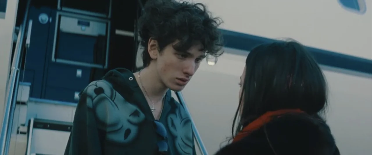 Anora (2024) movie still: medium — A metal staircase leads into the fuselage of a private jet on a tarmac. A young man and a woman stand close to…