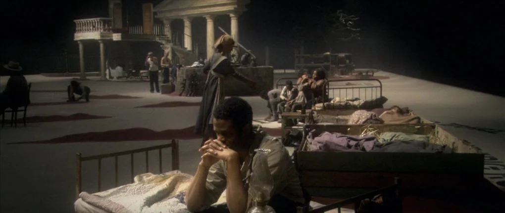 Manderlay (2005) movie still: wide — A sparse, open soundstage setup features minimal props on a wide, featureless floor. A man sits at the center…