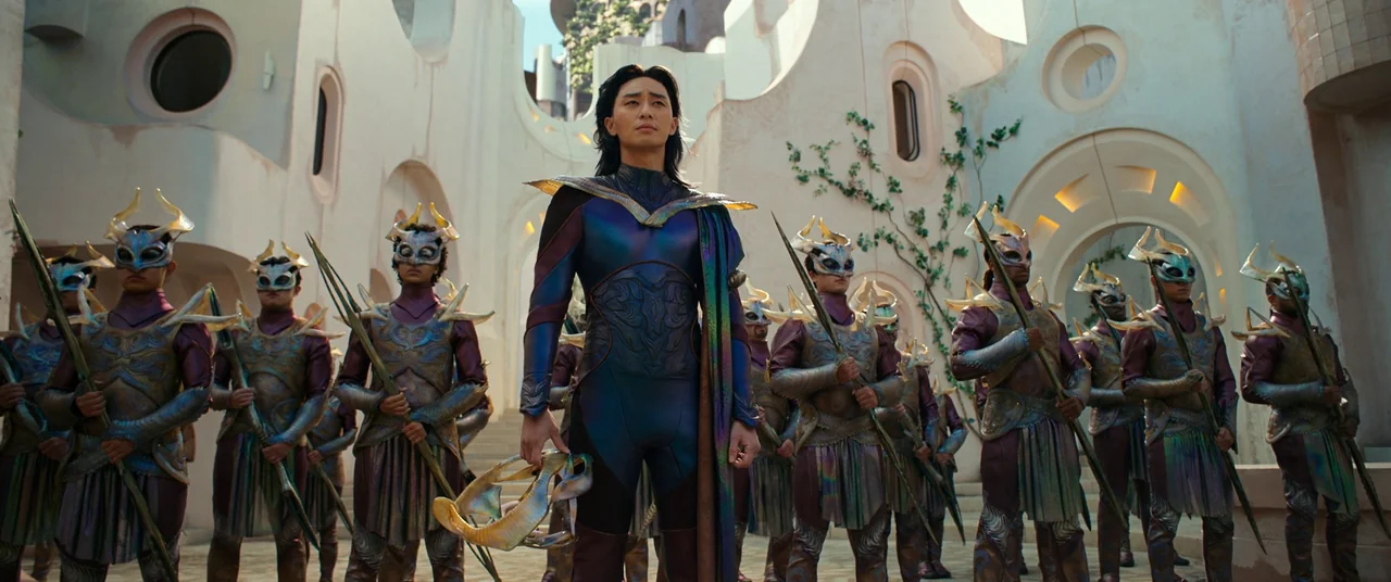 The Marvels (2023) movie still: fullbody — A light-colored stone courtyard with arched walls and rounded window cutouts. A central figure with long…