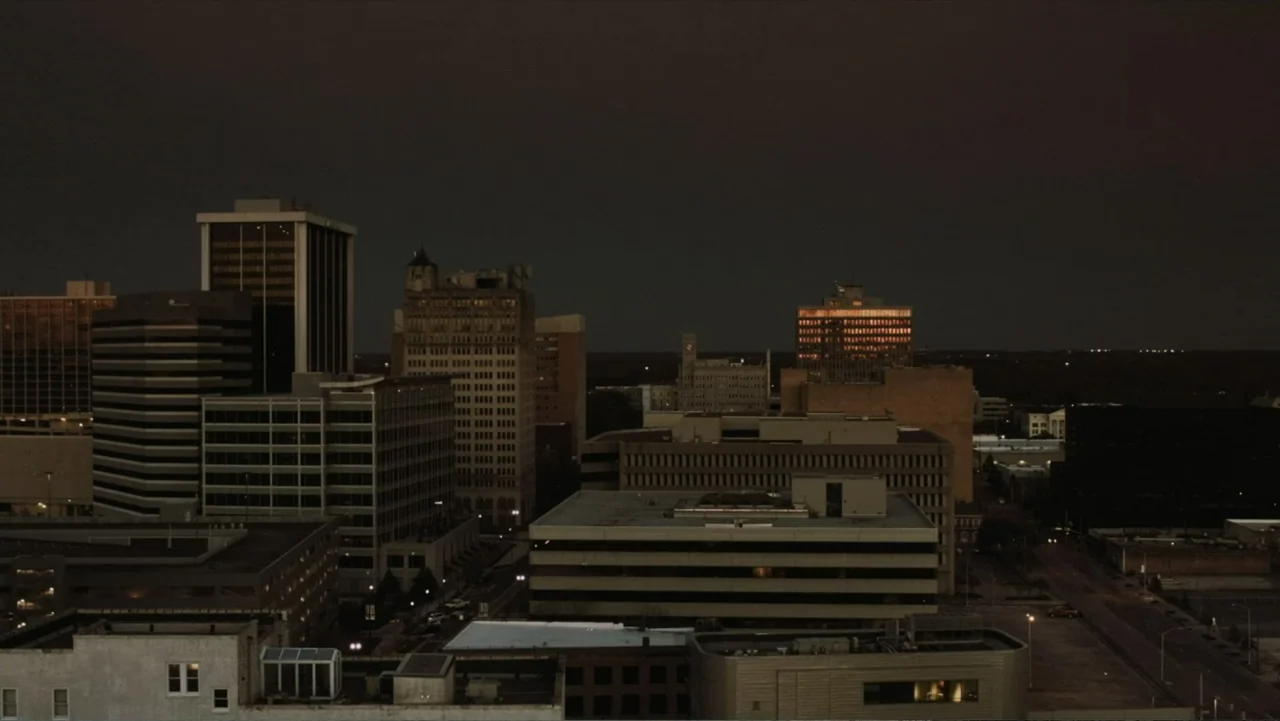 Death of a Child (2017) movie still: establishing — A high-angle view looks over a densely built urban cityscape at night. Multiple commercial…