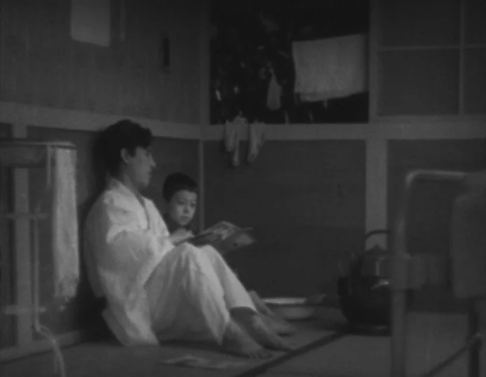Tokyo Chorus (1931) movie still: medium — A small Japanese room with tatami mats, wood-paneled walls, and sparse interior furnishings. A man and a…