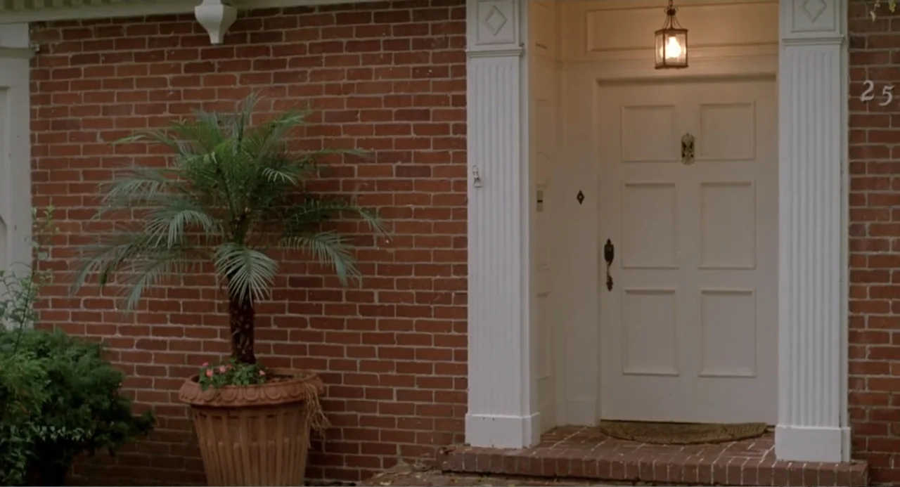 Dangerously Close (1986) movie still: wide — A red brick suburban house entrance features a white door with white trim. An outdoor lamp glows above…