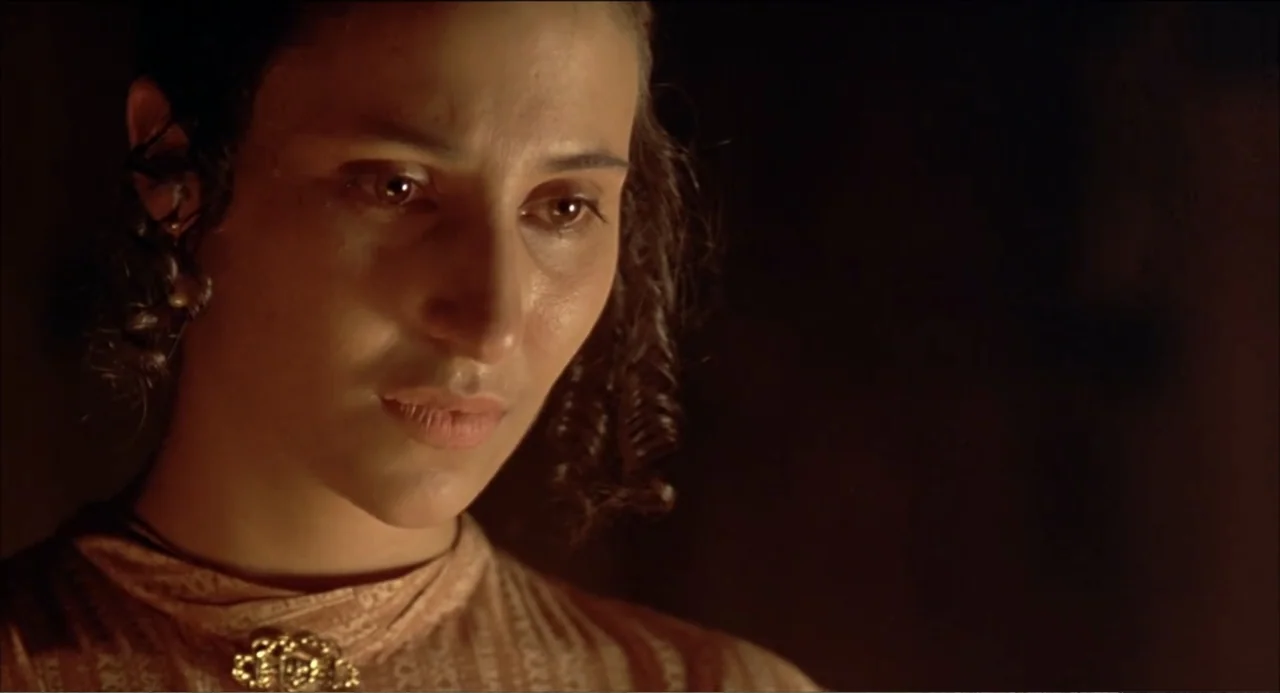 Like Water for Chocolate (1992) movie still: closeup — A dimly lit indoor space with dark, indistinct surroundings. A young woman with curly hair…
