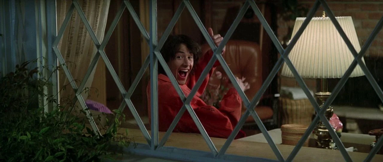 Bill and Ted’s Excellent Adventure (1989) movie still: medium — A man sits in a domestic space behind a decorative diamond-patterned interior window…