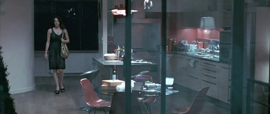 Boarding Gate (2007) movie still: wide — A modern open-concept apartment features a sleek kitchen area and a circular dining table. A woman walks…