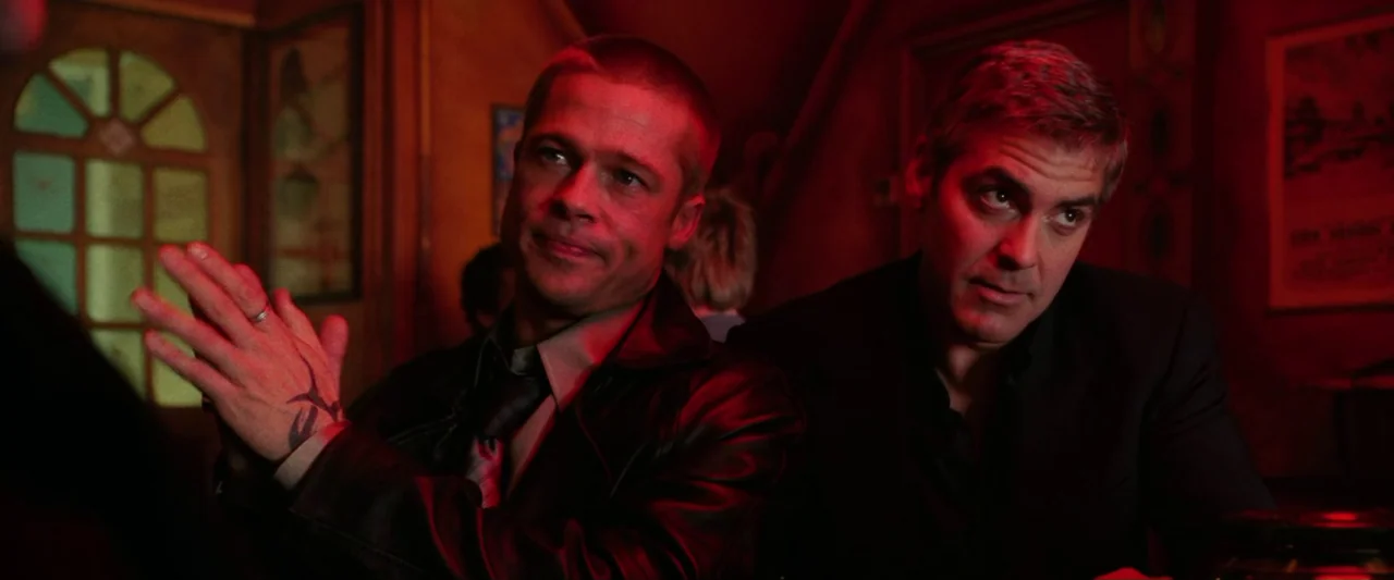 Ocean’s Twelve (2004) movie still: medium — Two men sit in a dimly lit bar interior bathed in saturated red illumination. They sit closely together…
