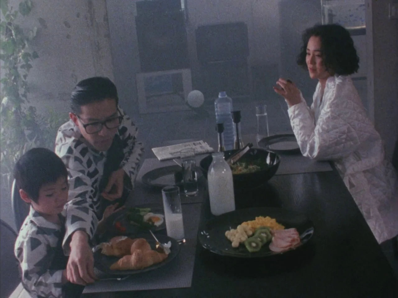 Tetsuo II: Body Hammer (1992) movie still: medium — A family sits at a dark table featuring plates of food and milk. A thin haze permeates the room…