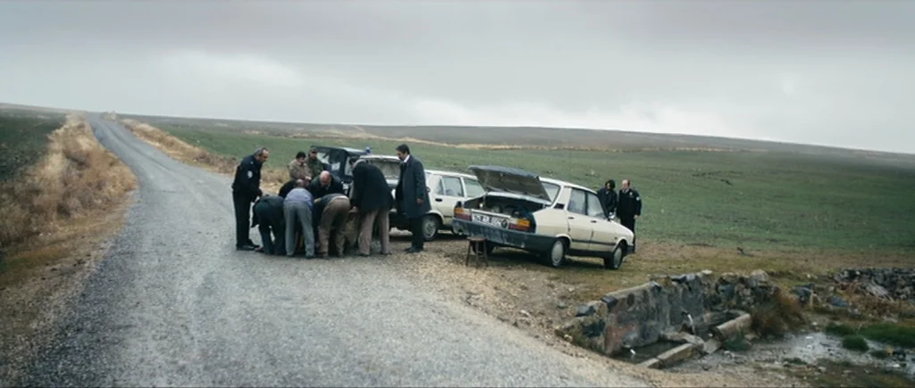 Once Upon a Time in Anatolia (2011) movie still: wide — A group of men and police officers stand near two parked cars on a road. They are gathered…