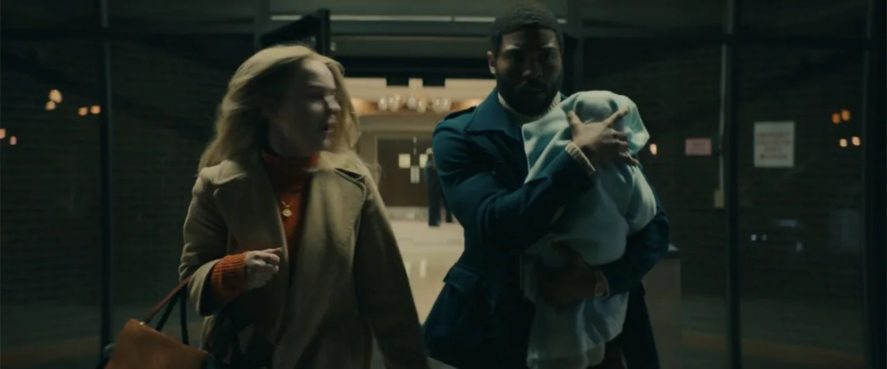 I'm Your Woman (2020) movie still: medium — A glass-walled building lobby at night with brick walls and subdued interior illumination. A man holding…