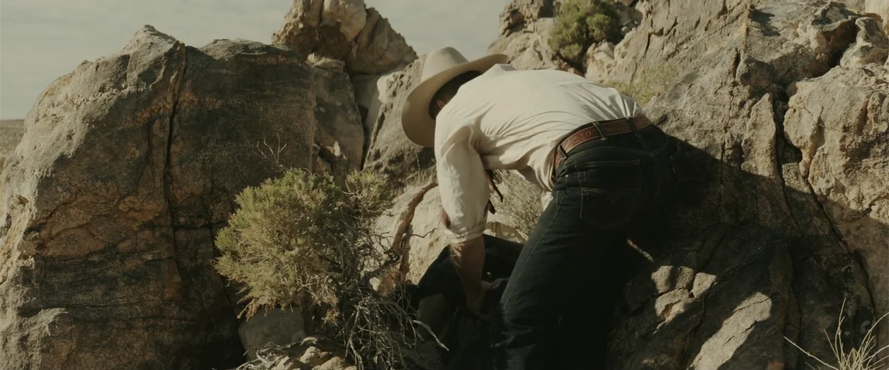 One Ranger (2023) movie still: medium — A man wearing a cowboy hat and denim jeans stands among jagged rock formations. He leans forward while…