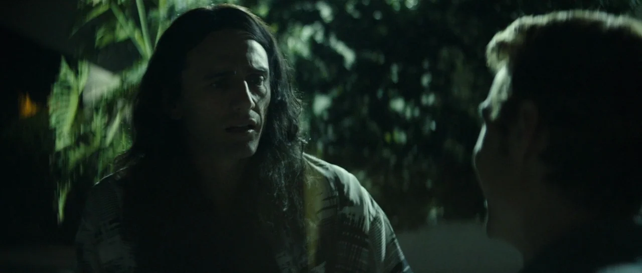 The Disaster Artist (2017) movie still: medium — An outdoor area at night with dense foliage blurred in the background. A man with long hair talks…