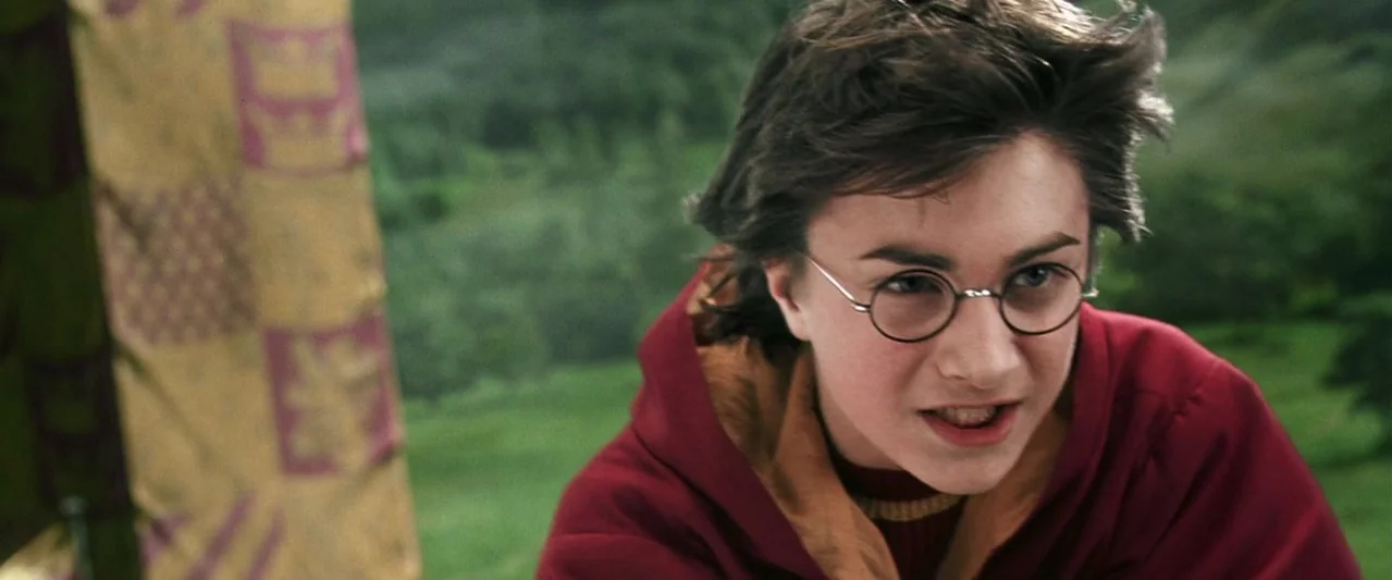 Harry Potter and the Chamber of Secrets (2002) movie still: closeup — A teenage boy wears a maroon robe while flying through the air. Blurred green…