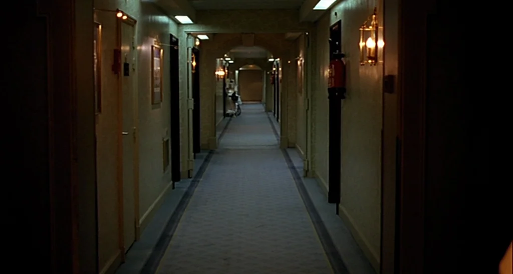Trouble Every Day (2001) movie still: establishing — A long, symmetrical hotel corridor stretches into the distance with closed doors on both sides.…