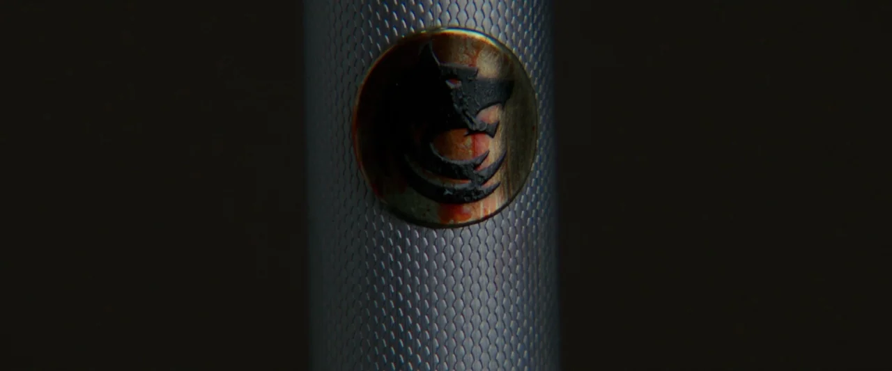 Hotel Artemis (2018) movie still: closeup — A close-up view shows a metallic cylindrical surface with a knurled texture. A circular emblem featuring…