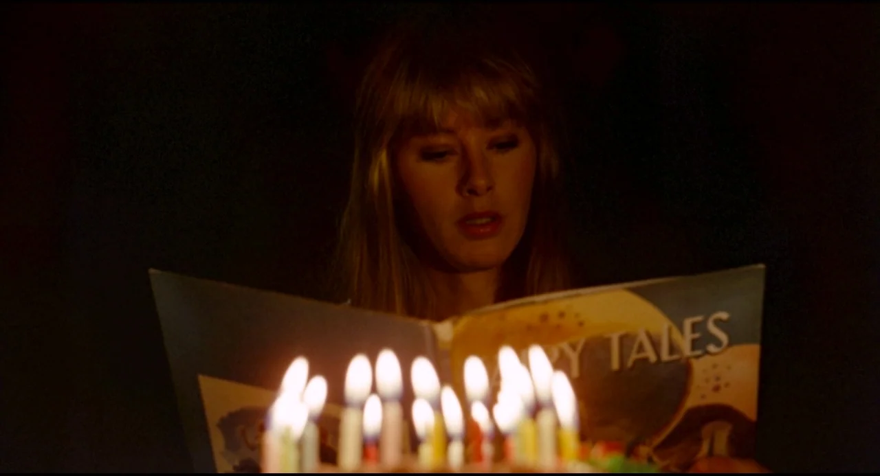 Olivia (1983) movie still: closeup — A woman reads a book titled Fairy Tales by the glow of many candles. The surrounding room is obscured by deep…