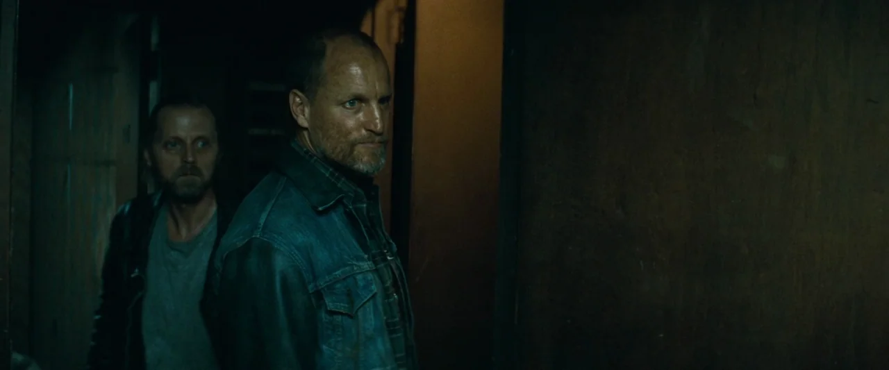 Out of the Furnace (2013) movie still: medium — A dark, dimly lit corridor with wood-paneled walls and low ambient illumination. Two men stand close…