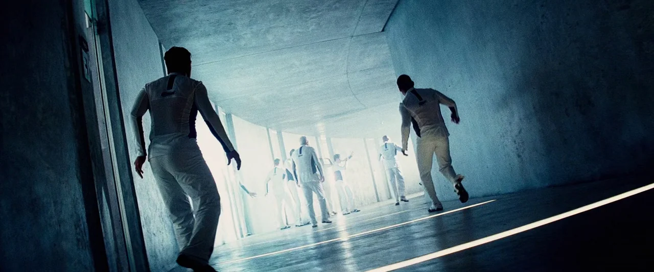 The Island (2005) movie still: wide — A long, smooth-walled, clinical corridor with integrated glowing floor light strips. Several figures in…