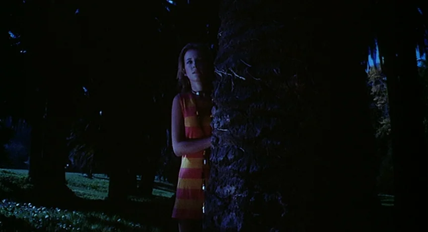5 Dolls for an August Moon (1970) movie still: medium — A dark night setting features dense trees and a grassy lawn background. A young woman in a…