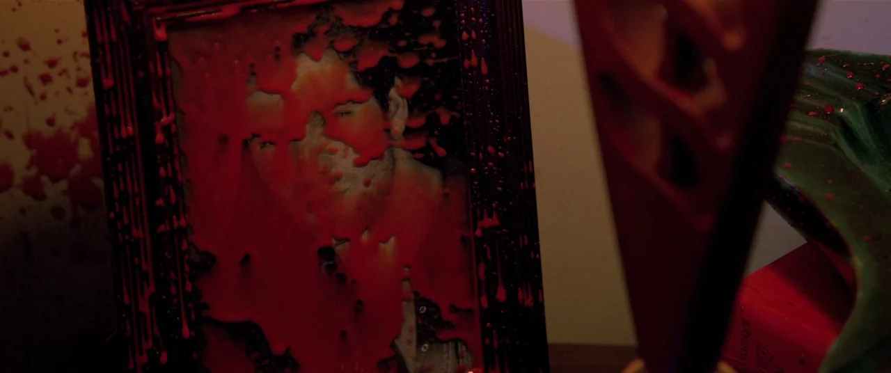 The Editor (2014) movie still: closeup — A close-up of a framed photograph covered in thick, dripping red liquid. Splatters of the substance are…