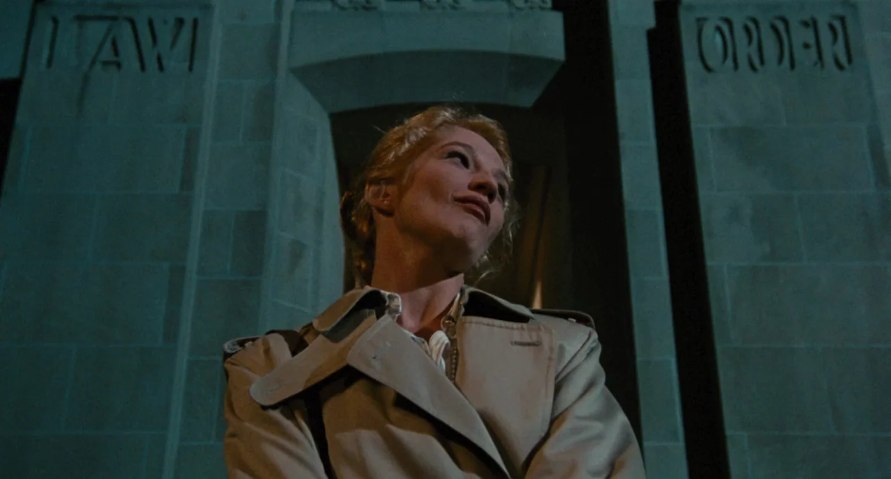 The Big Easy (1986) movie still: medium — A woman stands in front of a stone building with the words LAW and ORDER engraved on the facade. The…
