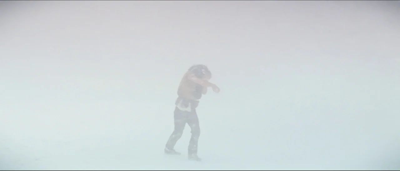 The NeverEnding Story (1984) movie still: wide — A featureless expanse of white snow and fog obscures the horizon. A man in a brown vest struggles…