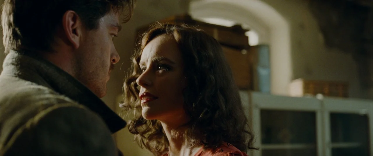 Phoenix (2014) movie still: medium — A dimly lit room with blurred architectural features like an arched opening in the background. A woman and a…