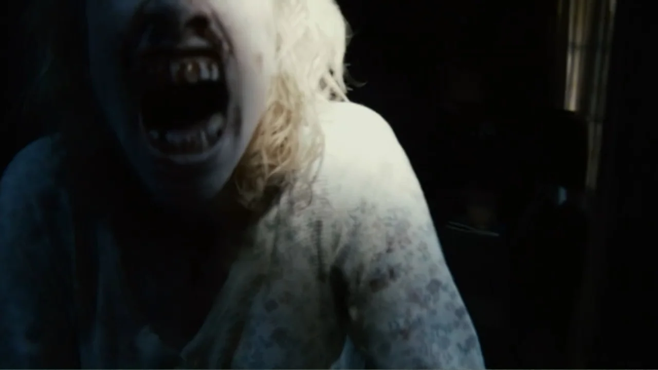 Quarantine (2008) movie still: closeup — A dark interior bedroom with minimal visible background details and heavy shadows. A woman with disheveled…