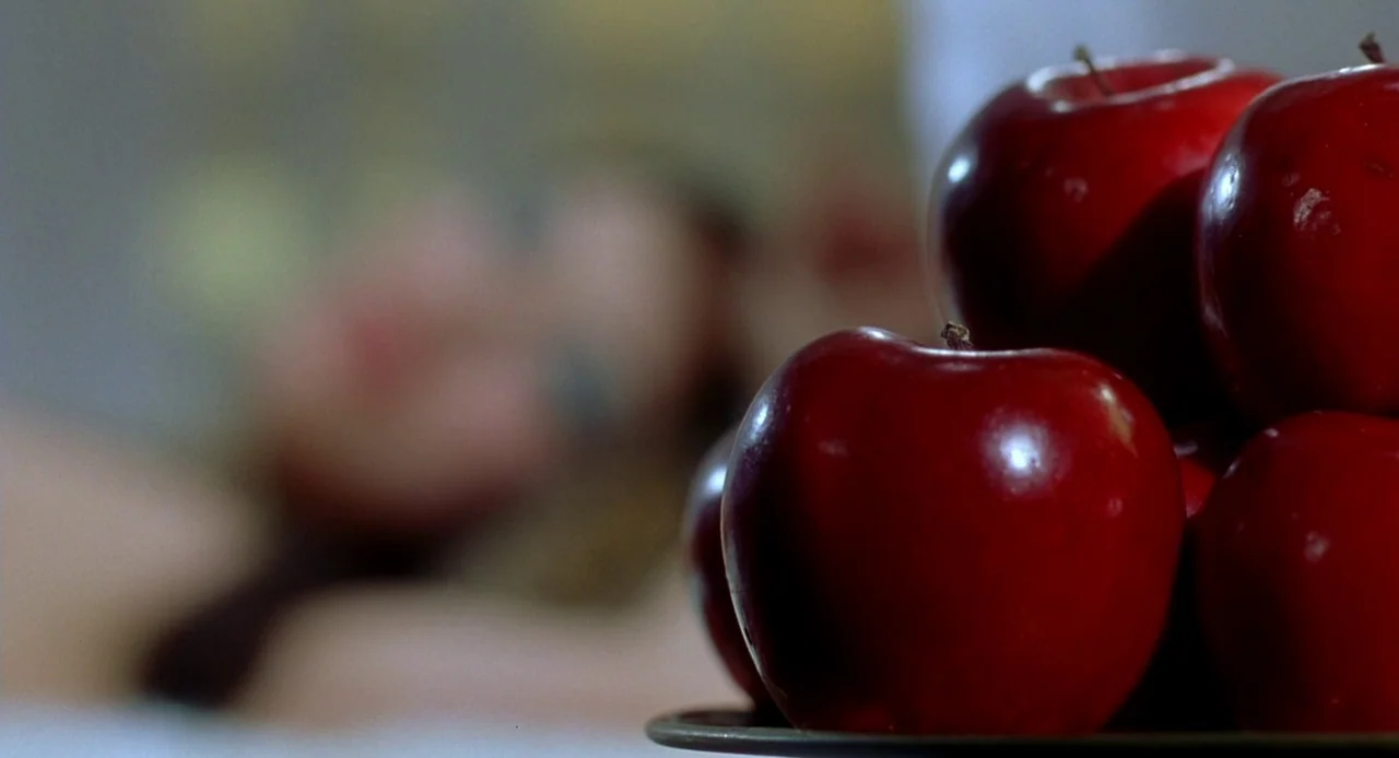 Viva (2007) movie still: closeup — A pile of polished red apples rests on a dark surface in the foreground. The background is completely out of…