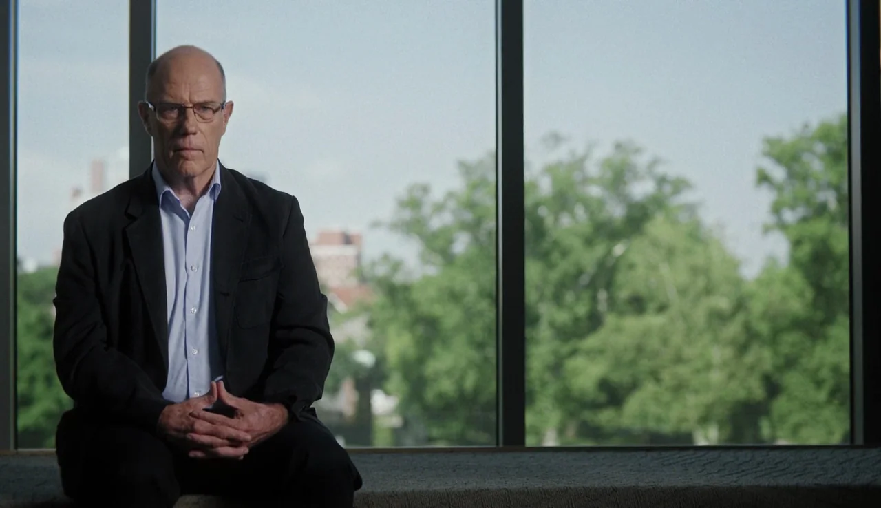 13th (2016) movie still: medium — A modern office space features a large window overlooking trees and city buildings. An elderly man in a suit sits…