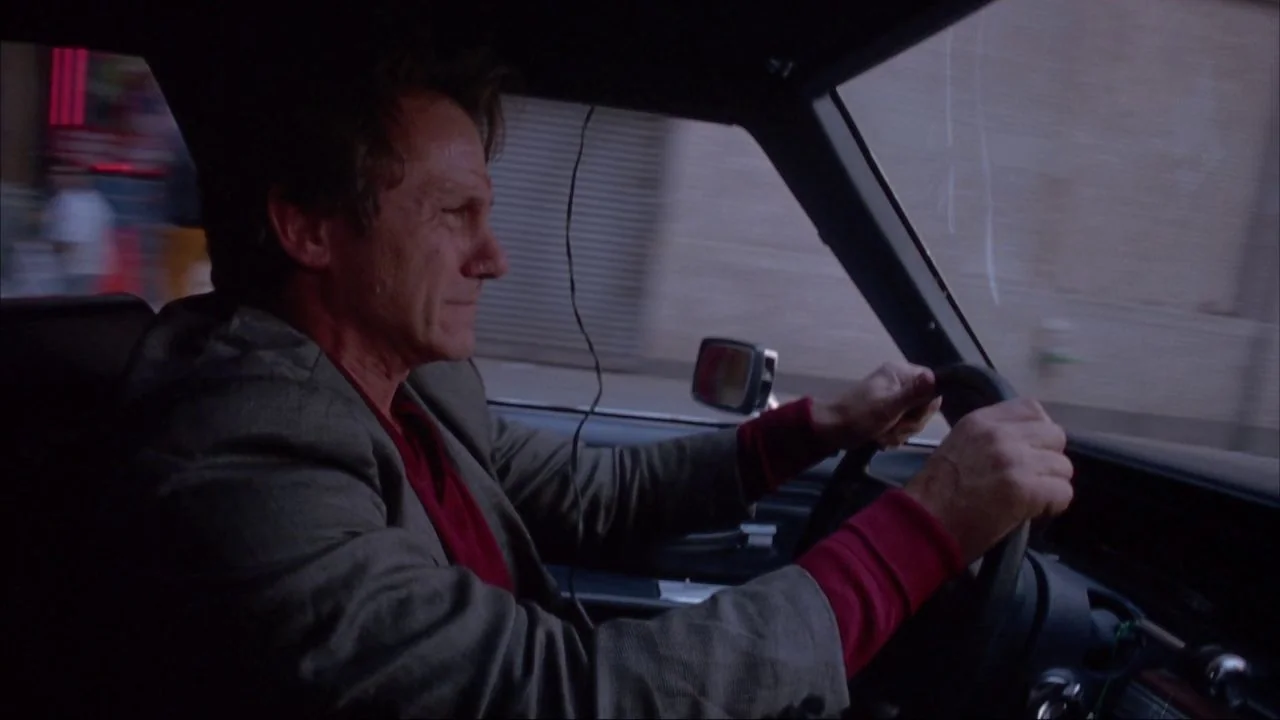 Bad Lieutenant (1992) movie still: medium — The interior of a moving car during daylight hours with blurry street scenery visible. A man in his…