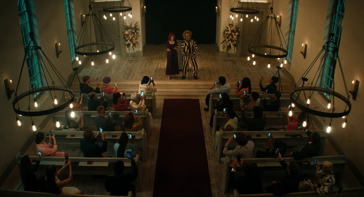 Beetlejuice Beetlejuice (2024) movie still: wide — A church interior with wooden pews facing a central altar and red runner carpet. An audience…