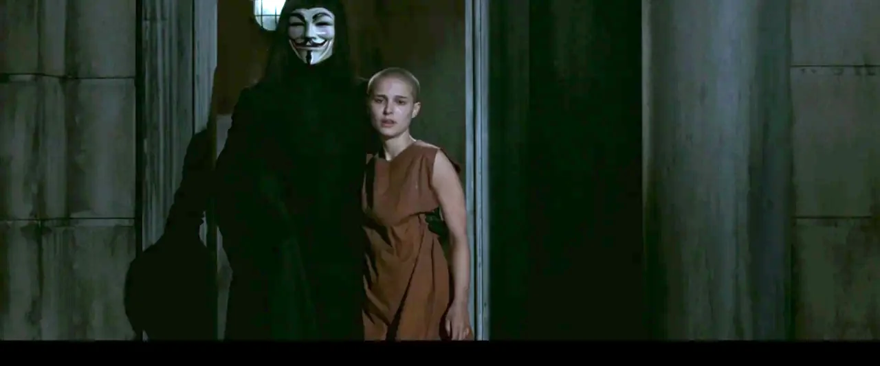 V for Vendetta (2006) movie still: medium — A dimly lit doorway frame shows dark masonry walls flanking a partially obscured interior space. A tall…