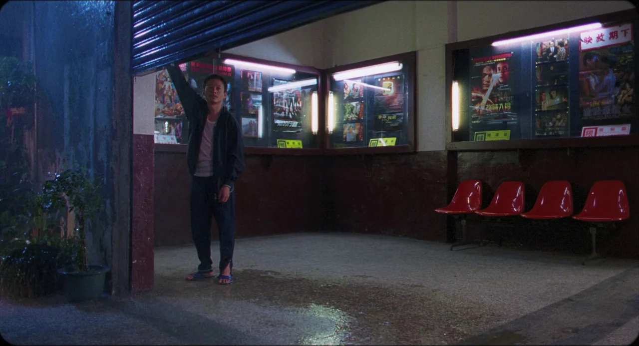 Goodbye, Dragon Inn (2003) movie still: fullbody — A nighttime view of a dimly lit movie theater foyer with dark floor tiles. A man stands under a…