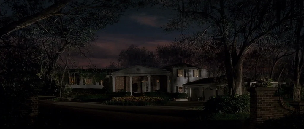 Cape Fear (1991) movie still: establishing — A two-story colonial style house sits at the end of a dark paved driveway. Large mature trees with…