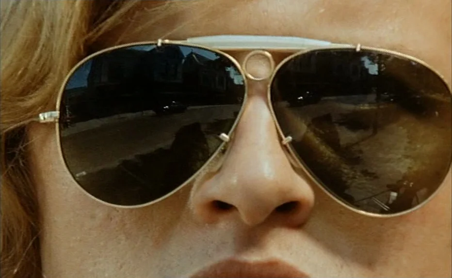 Turkish Delight (1973) movie still: closeup — An extreme close-up of a person's face wearing gold aviator sunglasses. The sunglasses reflect an…
