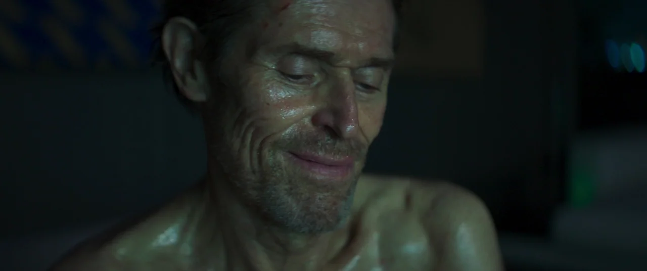 Inside (2023) (2023) movie still: closeup — A dimly lit interior space characterized by heavy shadow and cool-toned ambient light. A man with a thin…