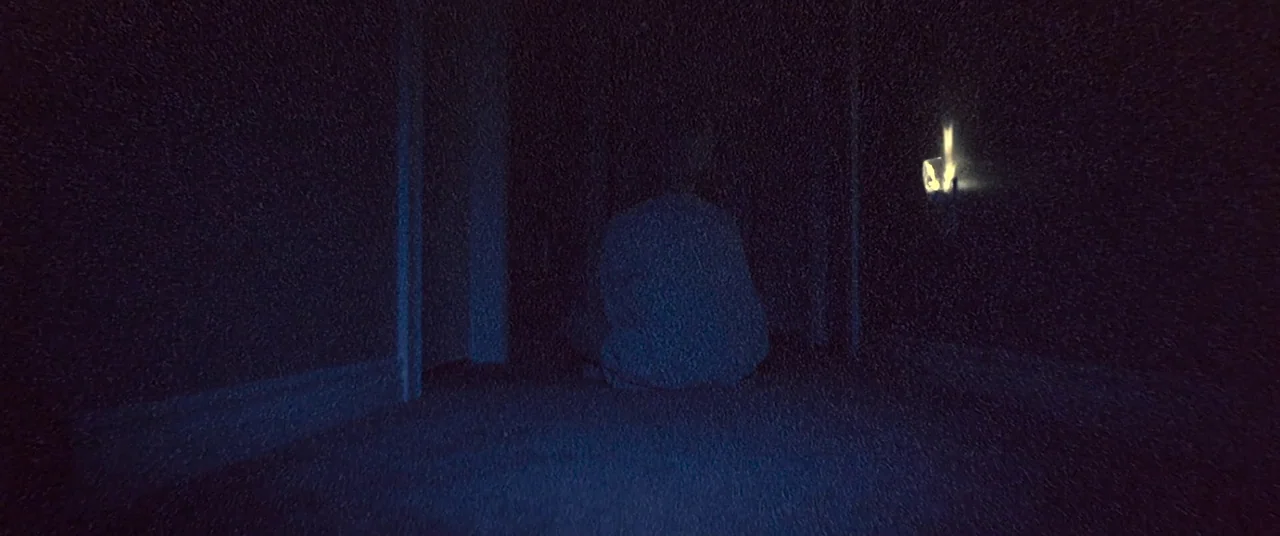 Skinamarink (2022) movie still: medium — A dark hallway with blue-tinted floor and walls under a dim light. A person sits on the carpeted floor with…