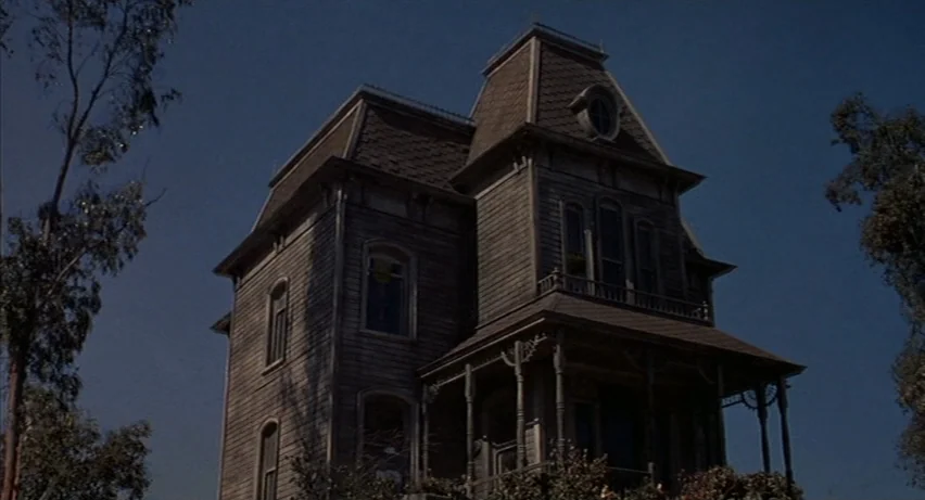 Psycho 2 (1983) movie still: establishing — A two-story Victorian mansion with weathered wood siding stands against a deep blue sky. Large trees…