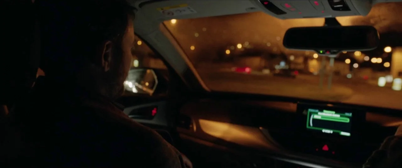 Happy New Year, Colin Burstead (2018) movie still: medium — The interior of a modern car at night with a driver facing forward. Blurred city lights…