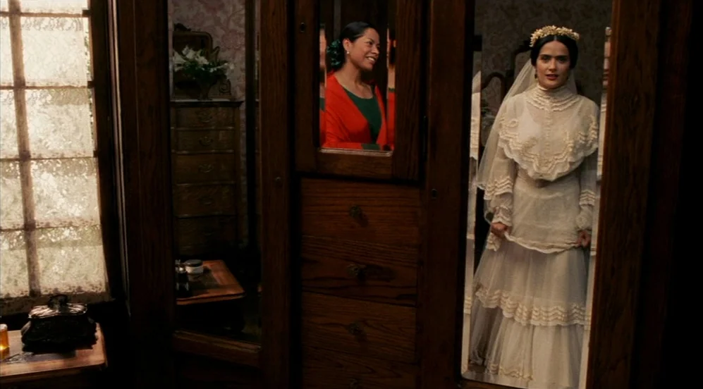 Frida (2002) movie still: medium — A wooden armoire with inset mirrors stands against a wall with faded floral wallpaper. A bride in a white wedding…