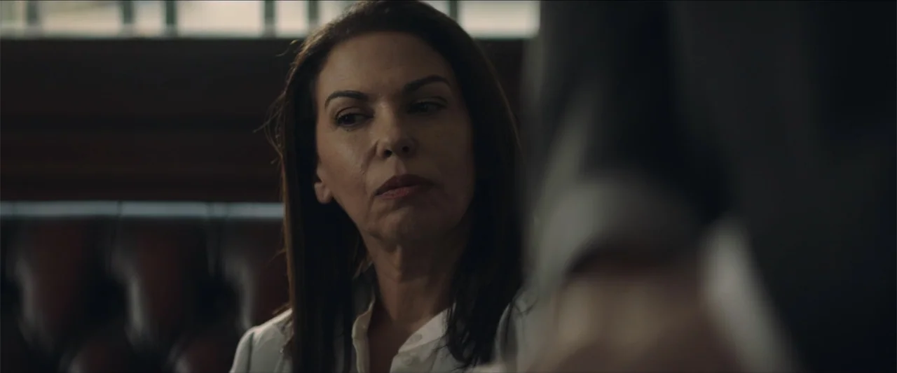 Redemption Day (2021) movie still: closeup — A dark wooden booth setting provides the backdrop for two people in conversation. The woman sits in the…