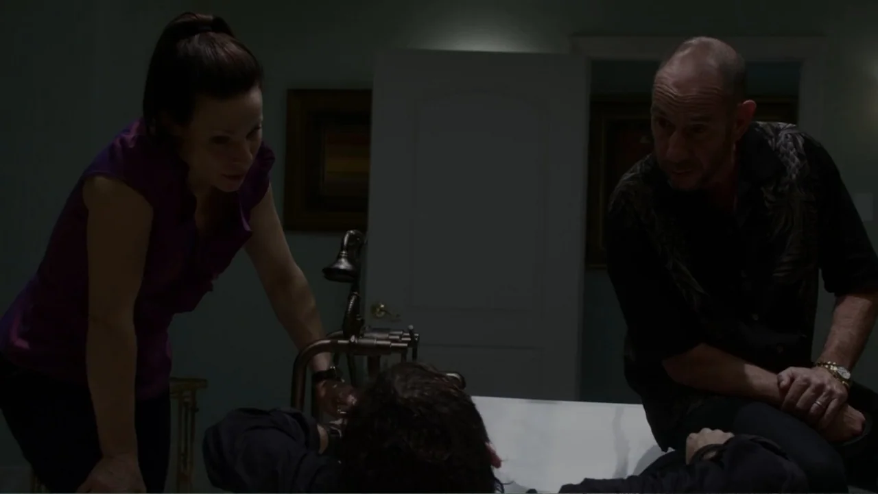 The Messenger (2015) movie still: medium — A dimly lit bathroom features a white porcelain tub and a doorway in the background. A woman and a man…