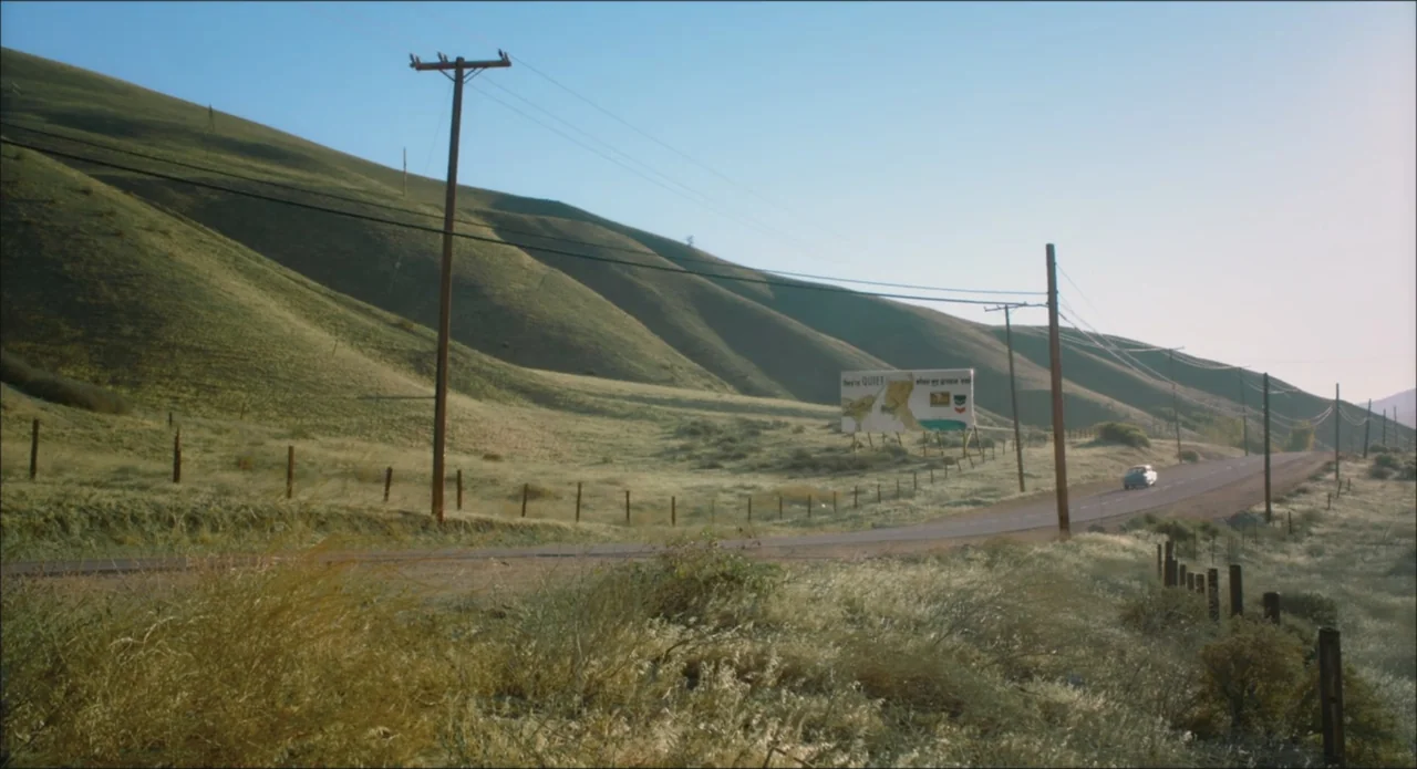 Big Brown Eyes (1936) movie still: wide — Rolling hills of dry grass stretch alongside a two-lane asphalt highway. A distant car drives toward the…