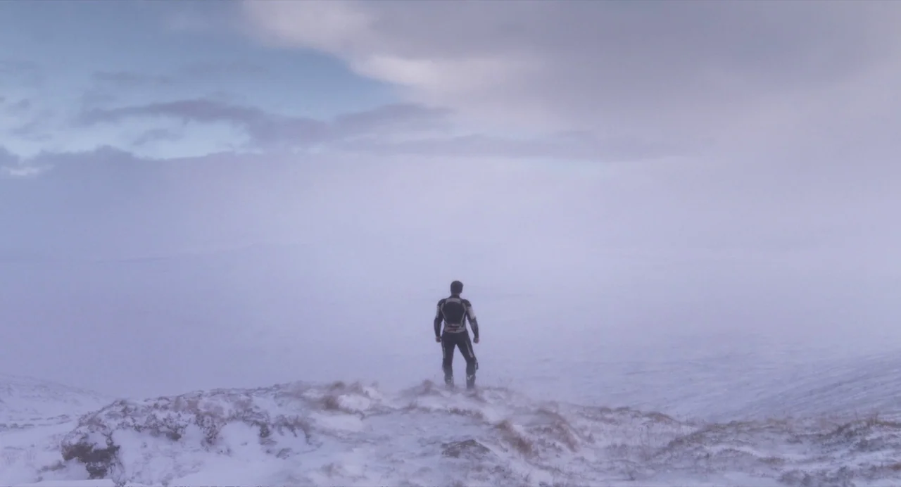 Under The Skin (2013) movie still: wide — A snowy mountain ridge stretches toward an expansive, mist-covered landscape under a pale sky. A lone…