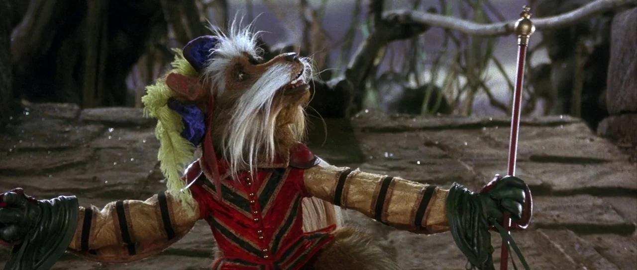Labyrinth (1986) movie still: medium — A puppet figure stands on a textured stone path surrounded by dark, blurred foliage. The character in ornate…